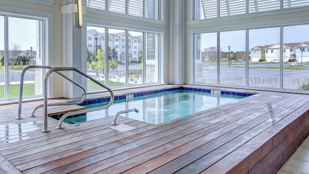 Eine Holzterrasse mit Pool, großen Fenstern und Blick auf Wohnhäuser.