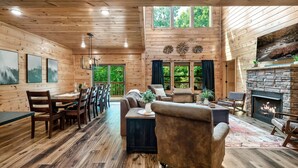 L’intérieur d’un chalet en bois comprend un coin repas, un salon, une cheminée et de grandes fenêtres.