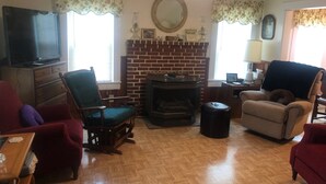 Una sala de estar con chimenea de ladrillo, dos sillones, un televisor y una mesa de centro de madera.