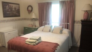 Un dormitorio con cama, mesita de noche, cómoda, lámpara y ventana con cortinas.