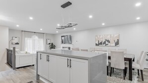 Una cocina moderna con armarios blancos, una isla central y un comedor con mesa y sillas.