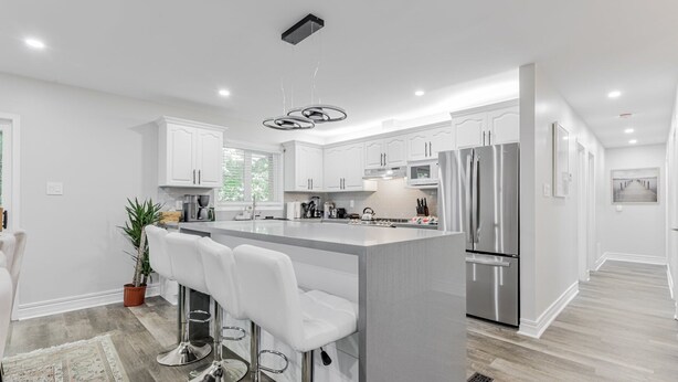 Una cocina moderna con armarios blancos, electrodomésticos de acero inoxidable y una isla central con taburetes de bar.