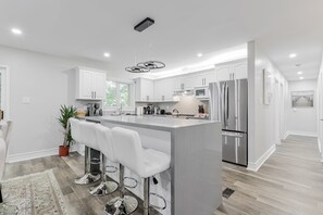 Una cocina moderna con armarios blancos, electrodomésticos de acero inoxidable y una isla central con taburetes de bar.