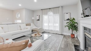 Una sala de estar moderna con un sofá blanco, una mesa de centro de vidrio y un gran ventanal con cortinas translúcidas.