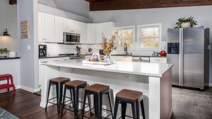 Una cocina moderna con armarios blancos, un refrigerador de acero inoxidable y una isla central con taburetes.