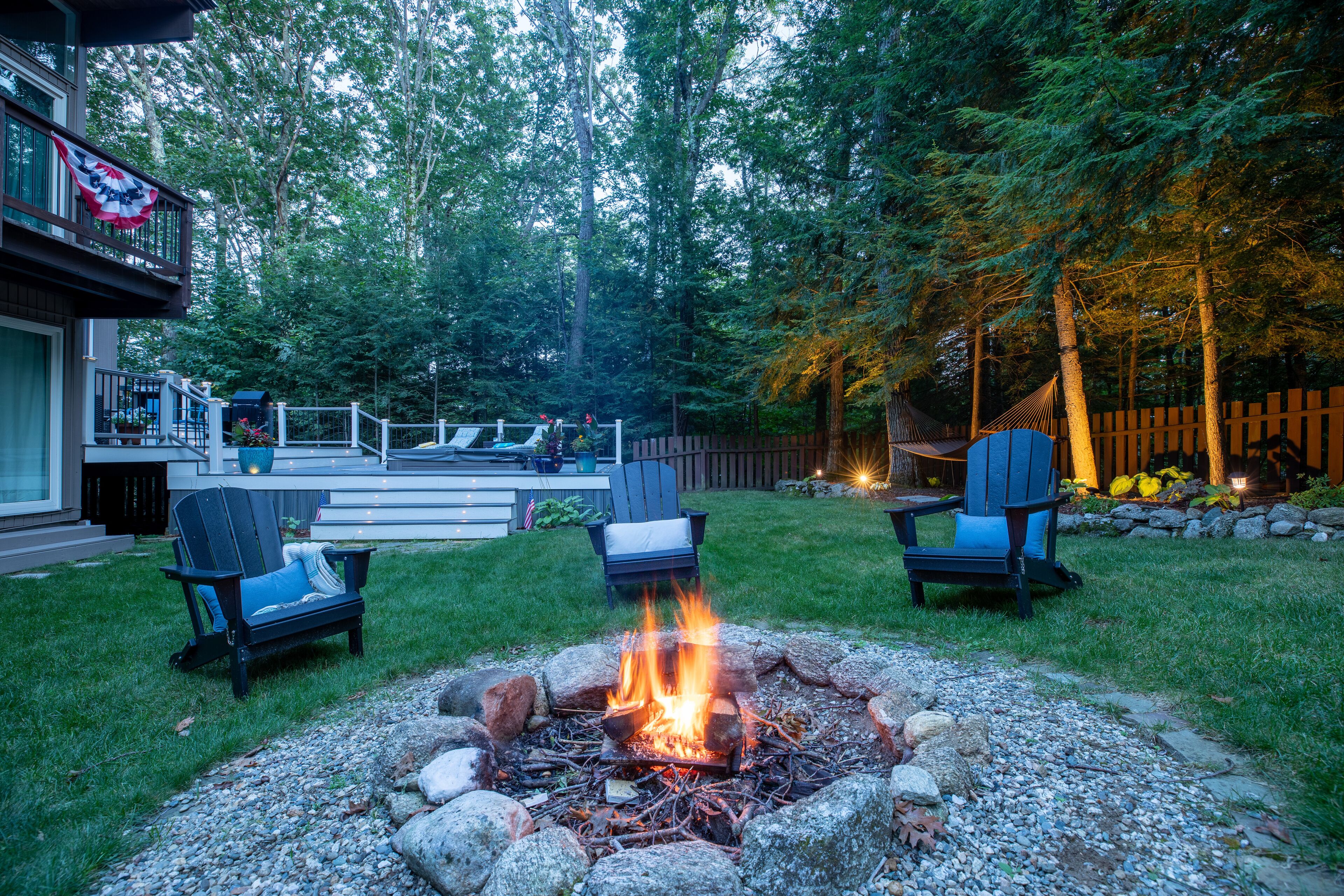 A backyard with a fire pit, two Adirondack chairs, and a deck.