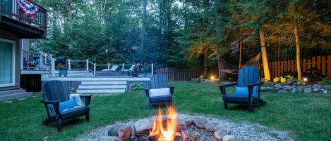 A backyard with a fire pit, two Adirondack chairs, and a deck.