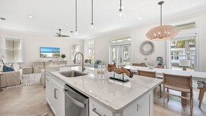 Una cocina amplia con una isla grande, luces colgantes modernas y un comedor con sillas de madera.