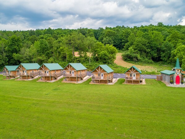 Une rangée de cabanes en bois aux toits verts, se dressant sur un fond de forêt dense et d’une route sinueuse.
