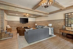 Un salon spacieux avec un grand canapé gris, un plancher en bois et un téléviseur fixé au mur.