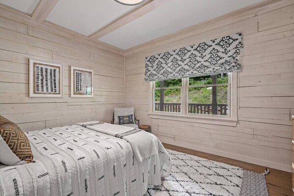 Une chambre à coucher avec un lit, une fenêtre donnant sur un beau paysage et deux tableaux encadrés accrochés au mur.