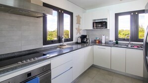 A modern kitchen with a stainless steel stove, a microwave, and a sink. There are decorative starfish on the windowsill and a blue towel hanging on the oven door. - Beachfront Luxury with Incredible Ocean Views (Worthing)