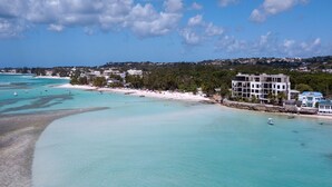 A coastal view with a beach, clear turquoise waters, and a building with multiple floors. - Beachfront Luxury with Incredible Ocean Views (Worthing)