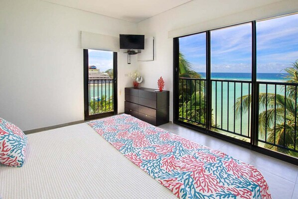 A bedroom with a bed, a dresser, a TV, and a balcony with a view of the ocean. - Beachfront Luxury with Incredible Ocean Views (Worthing)