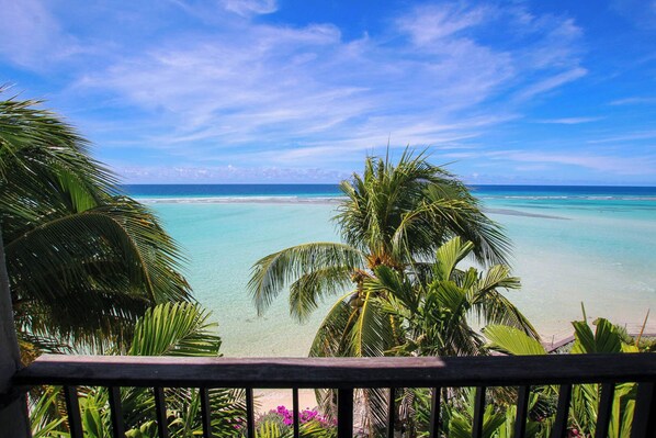 A tropical beach view with clear turquoise water, palm trees, and a wooden balcony railing. - Beachfront Luxury with Incredible Ocean Views (Worthing)