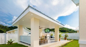 Une maison moderne dotée d’un patio couvert, d’une cuisine extérieure et d’un téléviseur à écran plat fixé au mur.