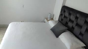 A neatly made bed with white linens and a dark headboard in a simple room with white walls.