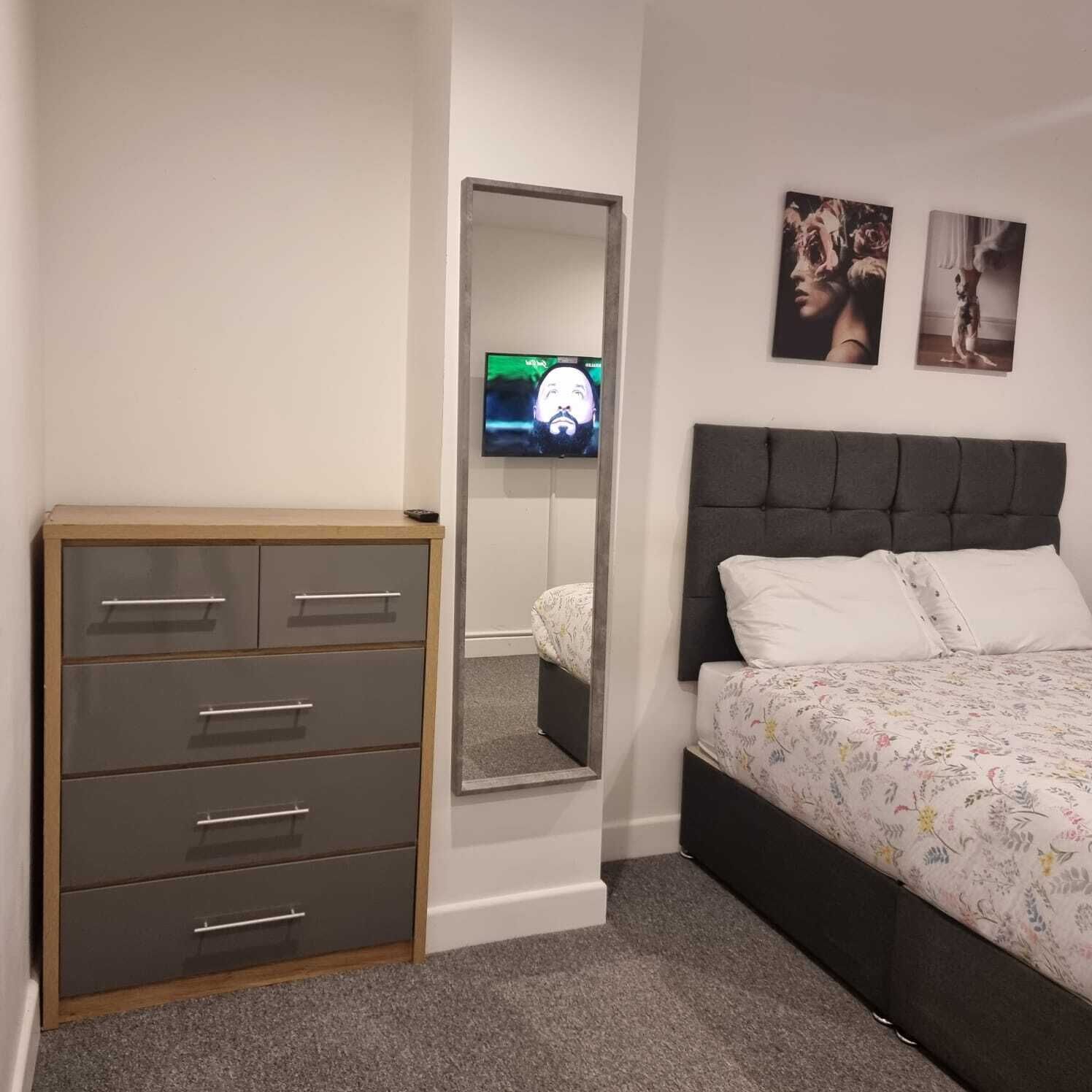 A bedroom with a bed, a dresser, a mirror, and two wall-mounted pictures.