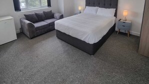 A bedroom with a large bed, a grey sofa, a small white radiator, and two bedside lamps. - Charming 4-bed House in Enfield North London (Enfield)