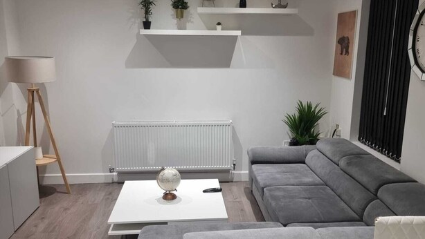A modern living room with a grey sofa, a coffee table, a lamp, and a radiator. - Charming 4-bed House in Enfield North London (Enfield)