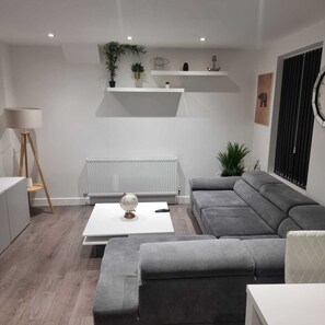 A modern living room with a grey sofa, a coffee table, a lamp, and a radiator. - Charming 4-bed House in Enfield North London (Enfield)