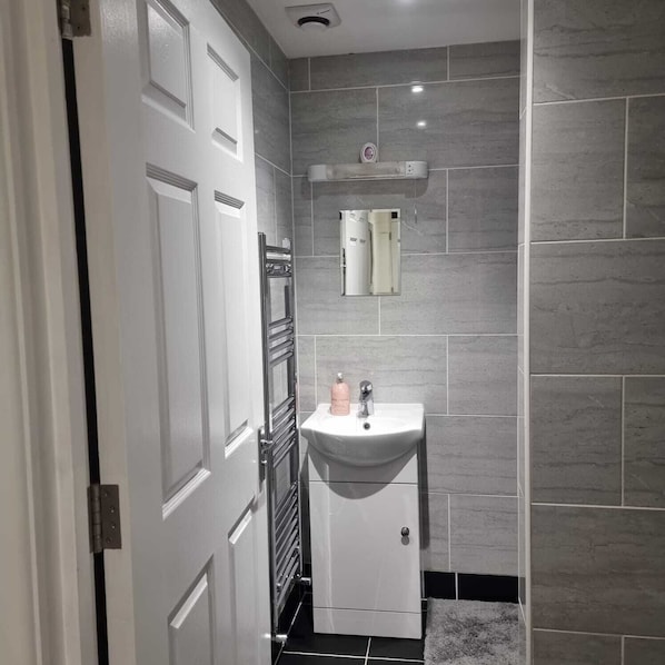 A bathroom with a white door, a white sink, a towel rack, and a mirror. - Charming 4-bed House in Enfield North London (Enfield)