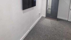 A room with a flat-screen TV mounted on the wall, a grey door, and a grey carpeted floor. - Charming 4-bed House in Enfield North London (Enfield)