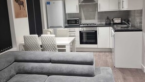 A modern kitchen with white cabinets, a stove, microwave, and a refrigerator. There is a dining area with a table and chairs. - Charming 4-bed House in Enfield North London (Enfield)