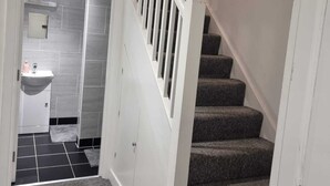 A staircase with a white handrail and carpeted steps leading to a bathroom with a white sink and tiled walls. - Charming 4-bed House in Enfield North London (Enfield)