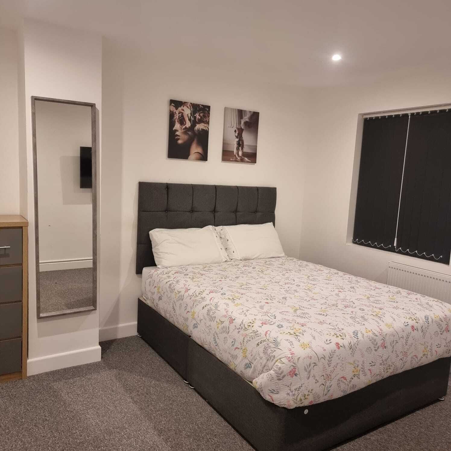 A bedroom with a bed, a dresser, a mirror, and two wall-mounted pictures.