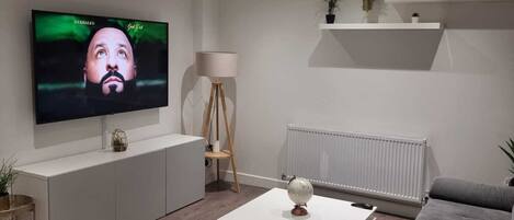 A modern living room with a flat-screen TV, grey sofa, white coffee table, and a radiator.