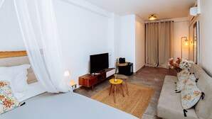 A modern hotel room with a bed, a TV, a sofa, and a small table.