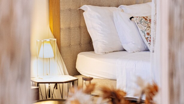 A bedroom with a bed, bedside table, lamp, and a vase with dried flowers.