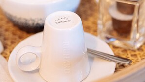 A table with a white cup labeled "Cafes Richard," a spoon, a small glass container, and a white teapot.