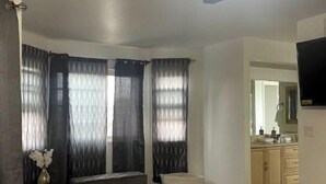 Et soveværelse med seng, ventilator, bænk og et vindue med gardiner.