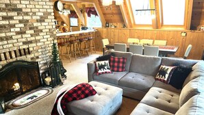 Un salon chaleureux avec une cheminée, un canapé et un coin repas équipé de tabourets de bar.