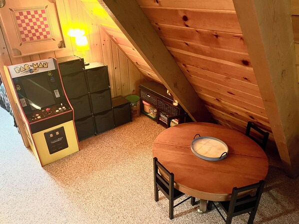 Una habitación de madera con una máquina arcade Pac-Man, una mesita con un bol y una silla.