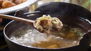 Primer plano de una sopa que se sirve con palillos, con una olla y una cuchara visibles al fondo.