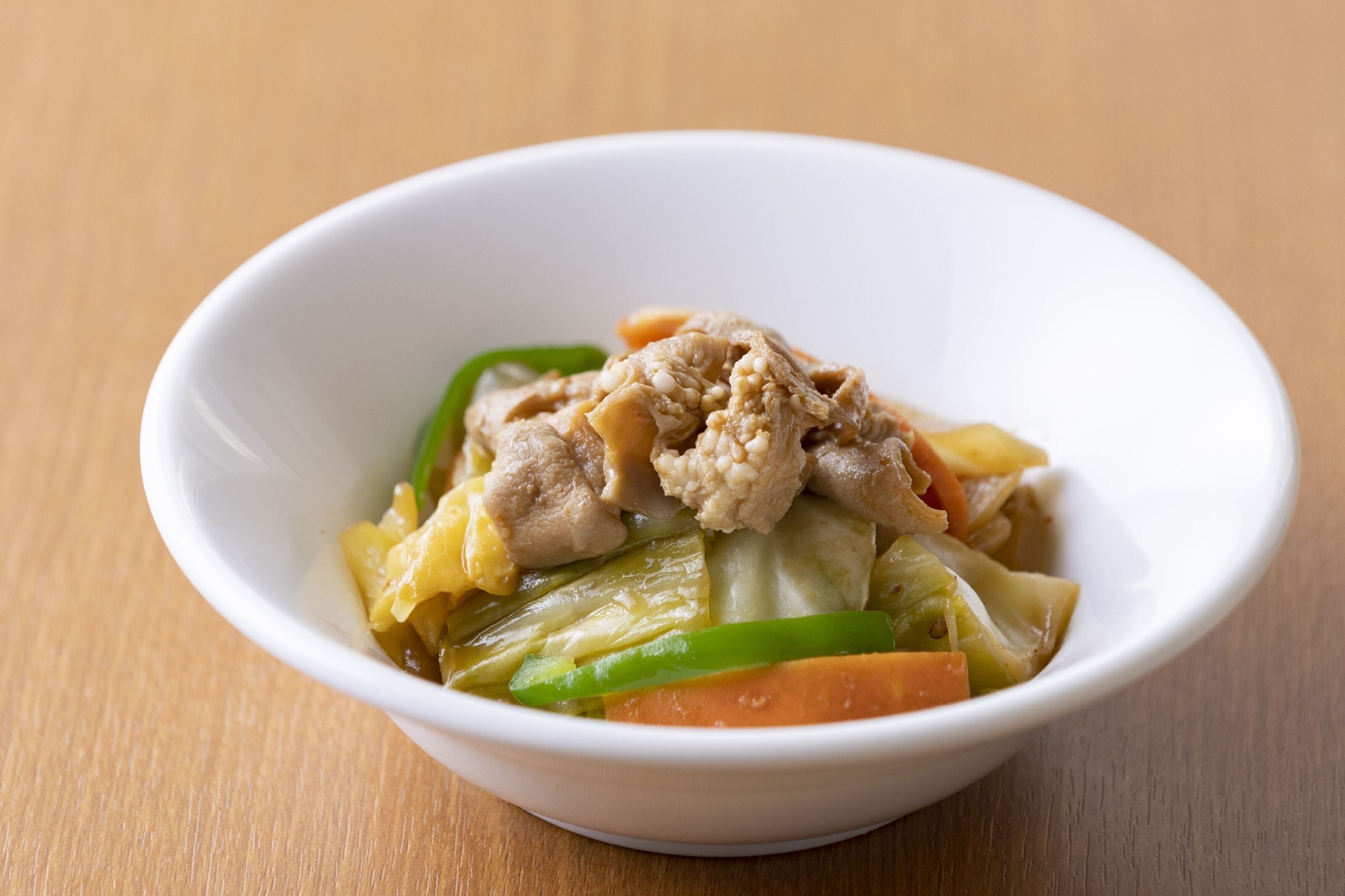 Un bol blanc contenant un plat composé de viande, de légumes et de morceaux d’ananas.