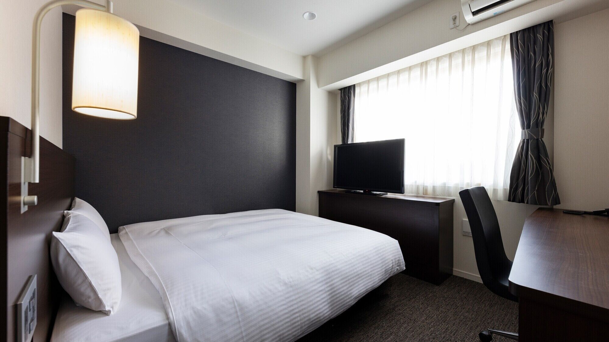Une chambre d’hôtel avec un lit, un bureau, une télévision et une fenêtre avec des rideaux.