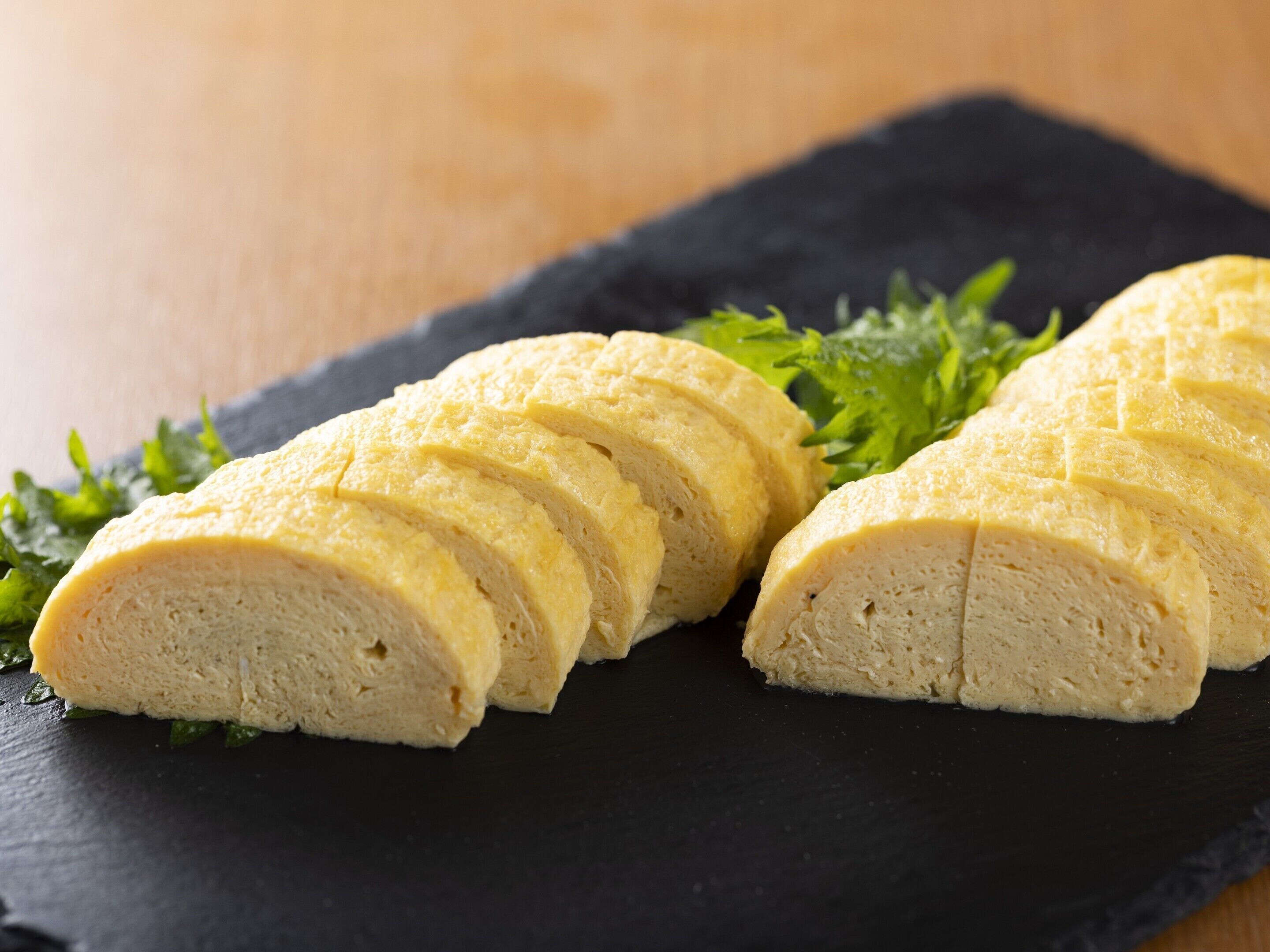 A loaf of bread sliced on a slate board with green garnish.