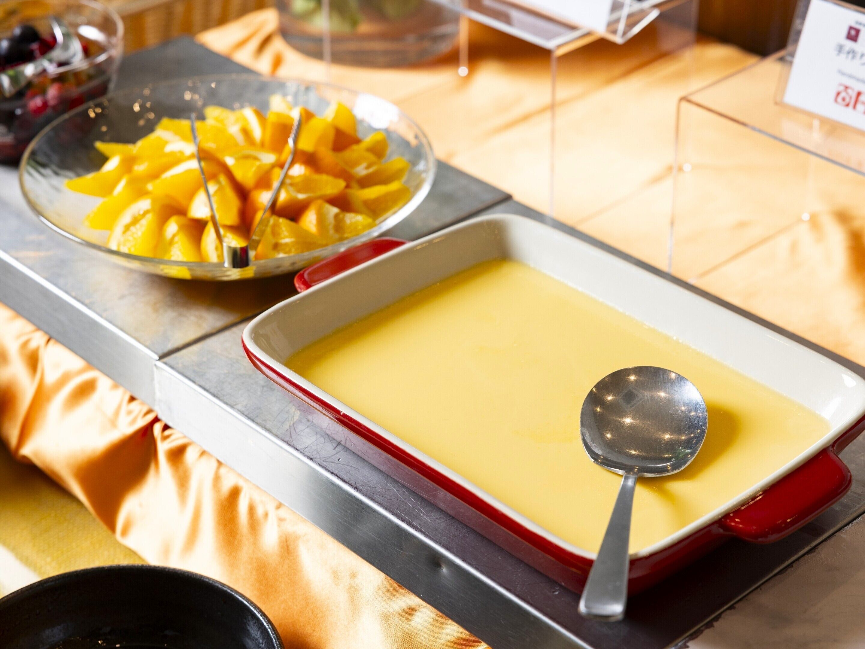 Una mesa de postres con un recipiente de crema pastelera y un bol de fruta cortada.