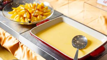 Una mesa de postres con un recipiente de crema pastelera y un bol de fruta cortada.