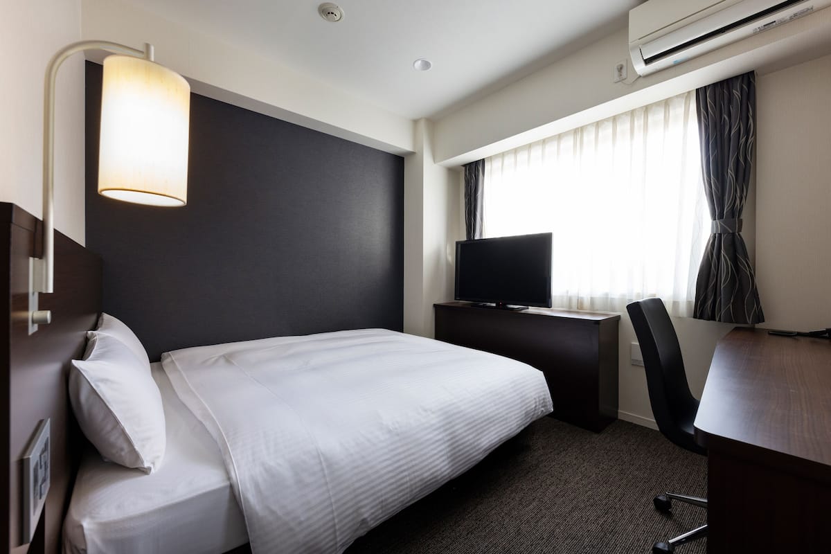 Habitación de hotel con cama, escritorio, silla, televisor y aire acondicionado.