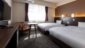 Hotellihuone, jossa on kaksi sänkyä, työpöytä, jossa on televisio, tuoli, pieni pöytä ja ilmastointilaite.