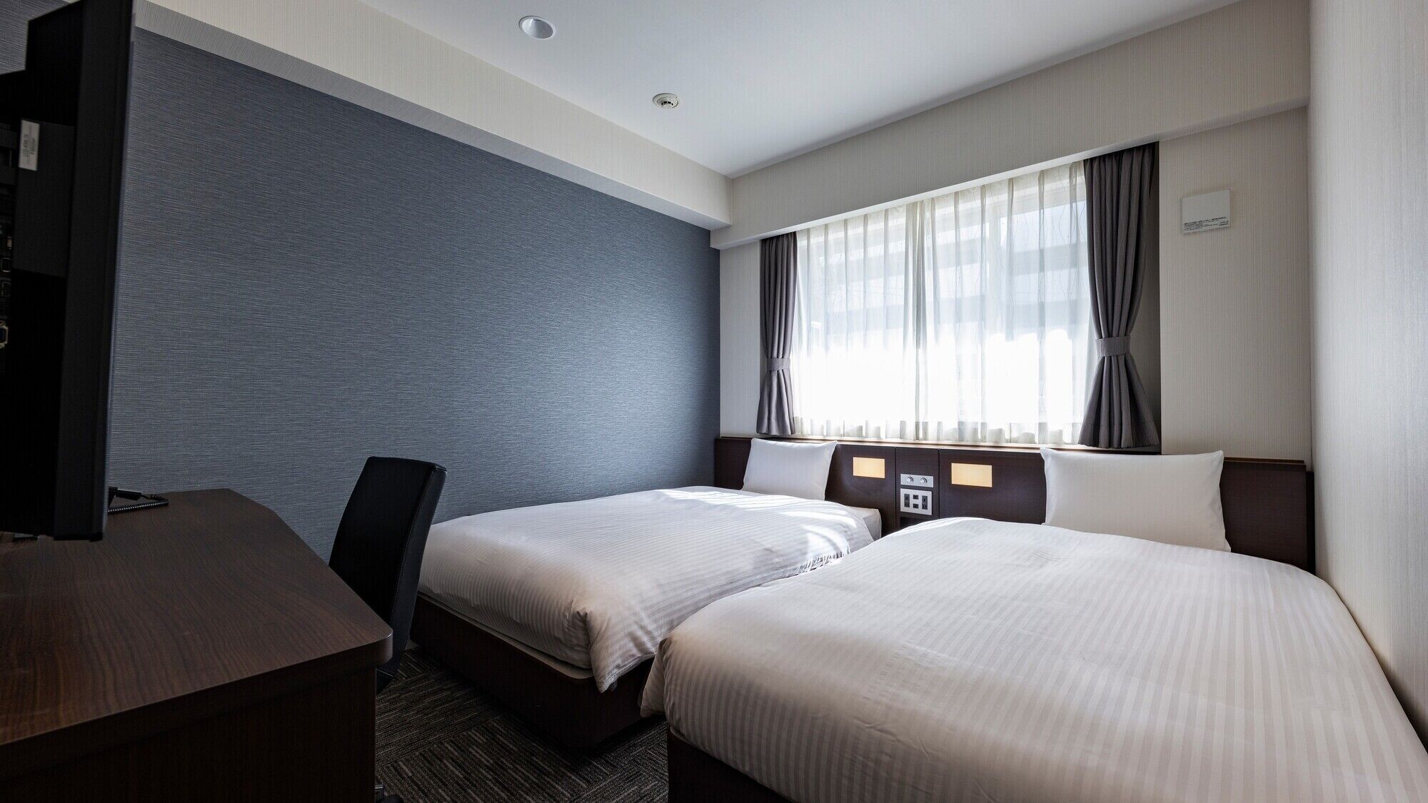 Une chambre d’hôtel avec deux lits, un bureau et une grande fenêtre avec des rideaux.
