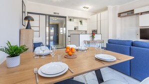 Een moderne eetruimte met een houten tafel voor vier personen, een blauwe bank en een keuken op de achtergrond.