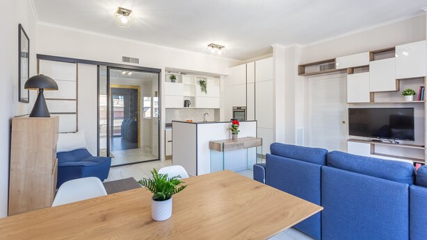 Een moderne woonkamer met een houten eettafel, een blauwe bank en een televisie.