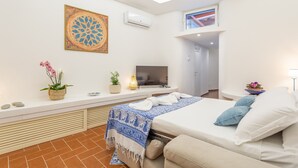 Una habitación de hotel moderna con una cama, un televisor, un adorno en la pared, una planta pequeña y una ventana con vistas.