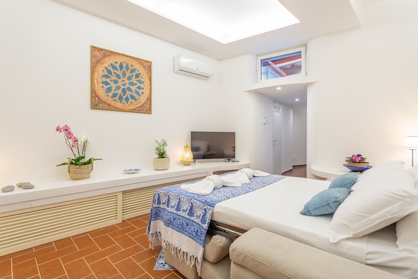 Quarto de hotel moderno com uma cama, televisão, um objeto decorativo na parede, uma pequena planta e uma janela com vista.